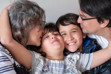 A joyful family of four sharing a warm embrace, highlighting love and togetherness indoors.