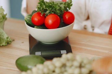 Colorful fresh vegetables including tomatoes and cucumbers on a kitchen scale for healthy eating.